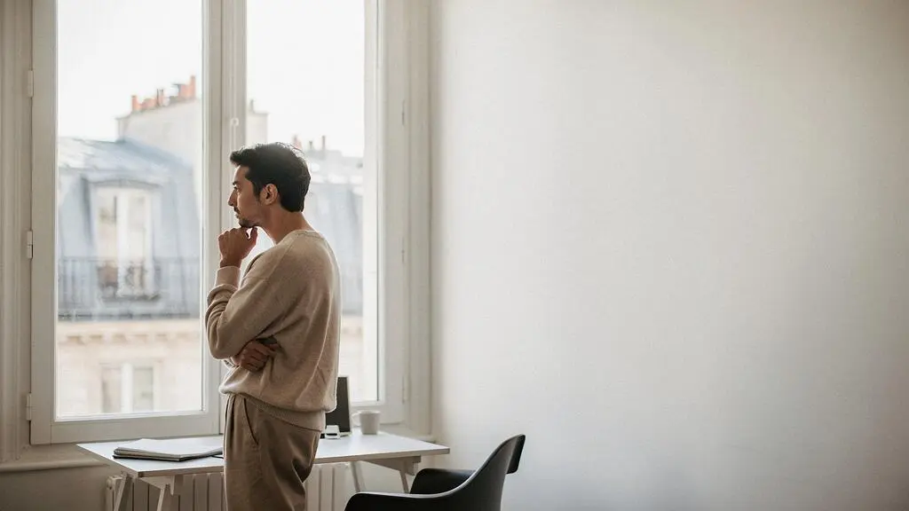 Redacteur pensif regardant par une fenetre haussmannienne parisienne, symbolisant l'ecoute de l'audience avant d'ecrire un contenu